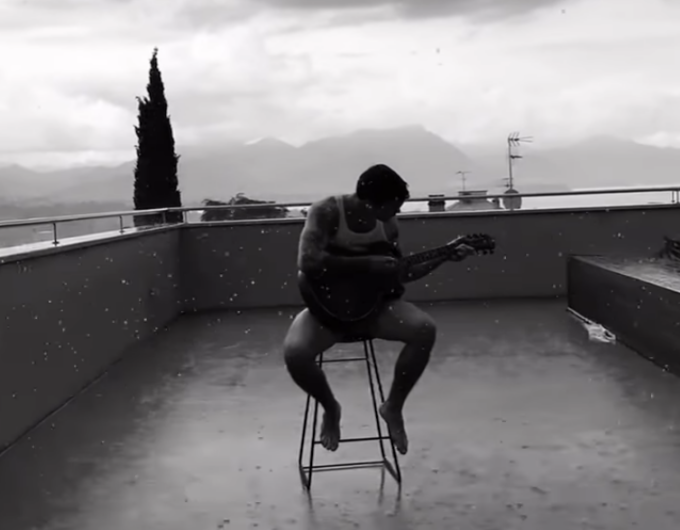 Blanco suona la chitarra sotto la pioggia